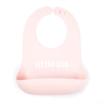 Bella Tunno "Little Sis" Wonder Bib in pink, featuring a generous catch pocket and adjustable neck closure, available at Be Charmed.