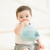 Baby wearing Bella Tunno Baby Bro Wonder Bib in soft blue, featuring a "baby bro" design, adjustable neck, and a catch pocket, made from BPA-free silicone, available at Be Charmed