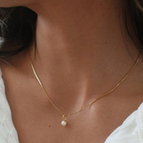 Gold necklace with a pearl pendant on a person wearing a white top. Available at Be Charmed