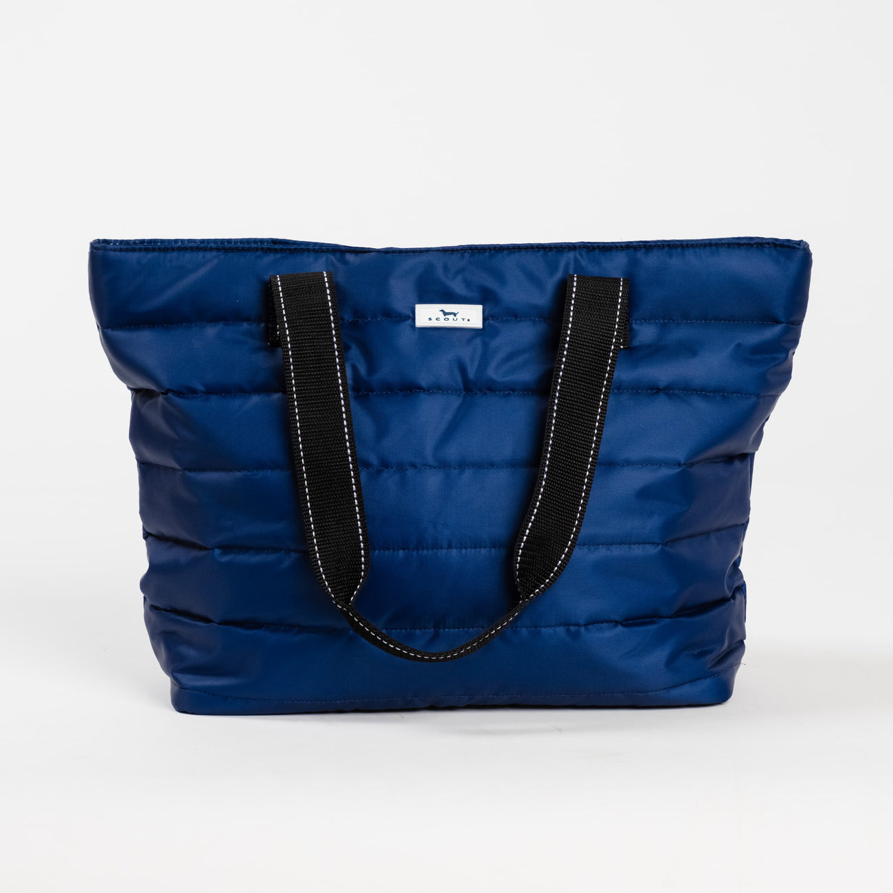 Navy Puffer SCOUT Layover Tote – quilted puffer travel tote (19″ W × 13″ H × 5.5″ D), interior zipper compartments, reinforced bottom, folds flat. Available at Be Charmed