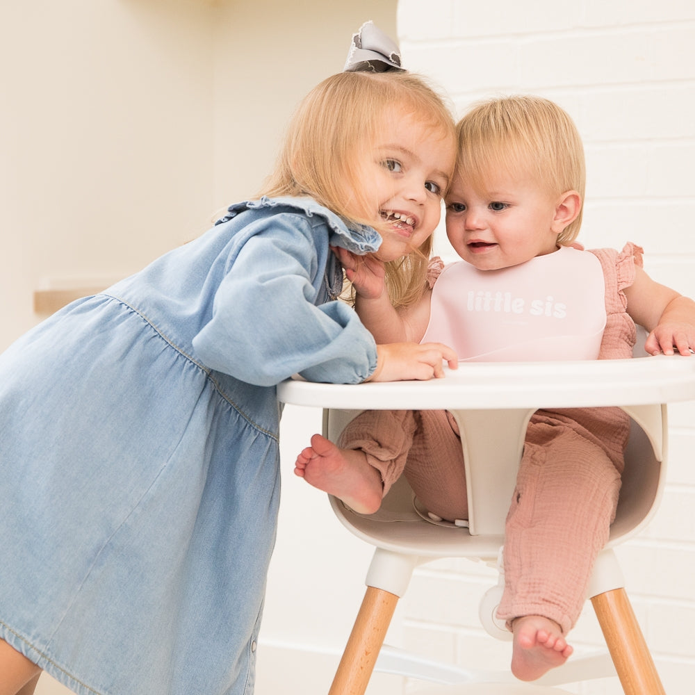 Bella Tunno Little Sis Wonder Bib pictured on baby in highchair with sister