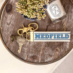 Rustic Marlin Medfield MAVarsity Font Keychain pictured on a wooden tray