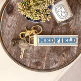 Rustic Marlin Medfield MAVarsity Font Keychain pictured on a wooden tray