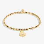 Gold bracelet with a heart-shaped charm on a white background. Available at Be Charmed