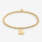 Gold bracelet with a heart-shaped charm on a white background. Available at Be Charmed