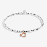 Silver bracelet with a heart-shaped rose gold charm on a white background. Available at Be Charmed