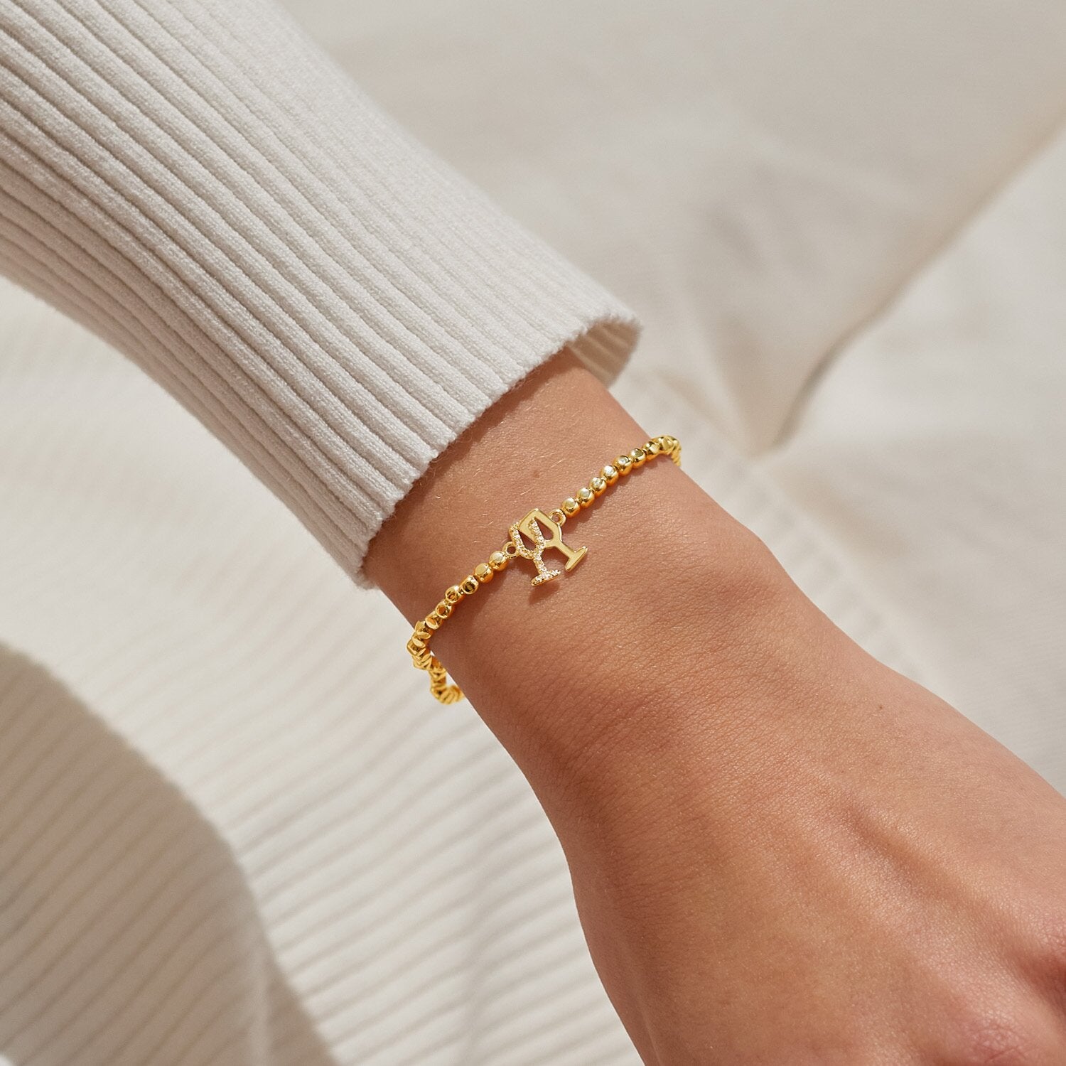 Gold bracelet with a champagne charm on a wrist against a neutral background. Available at Be Charmed
