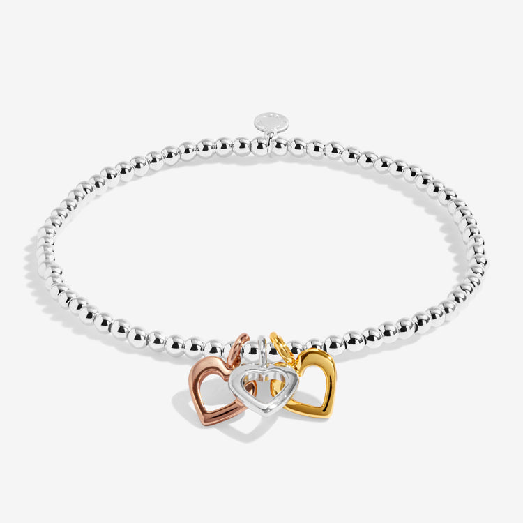 Silver bracelet with three heart-shaped charms in gold, rose gold, and silver on a white background. Available at Be Charmed