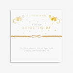 A gold-colored bracelet labeled 'A Littles & Co. Bride To Be' with a pretty bow charm, presented on a white card with gold accents and text.