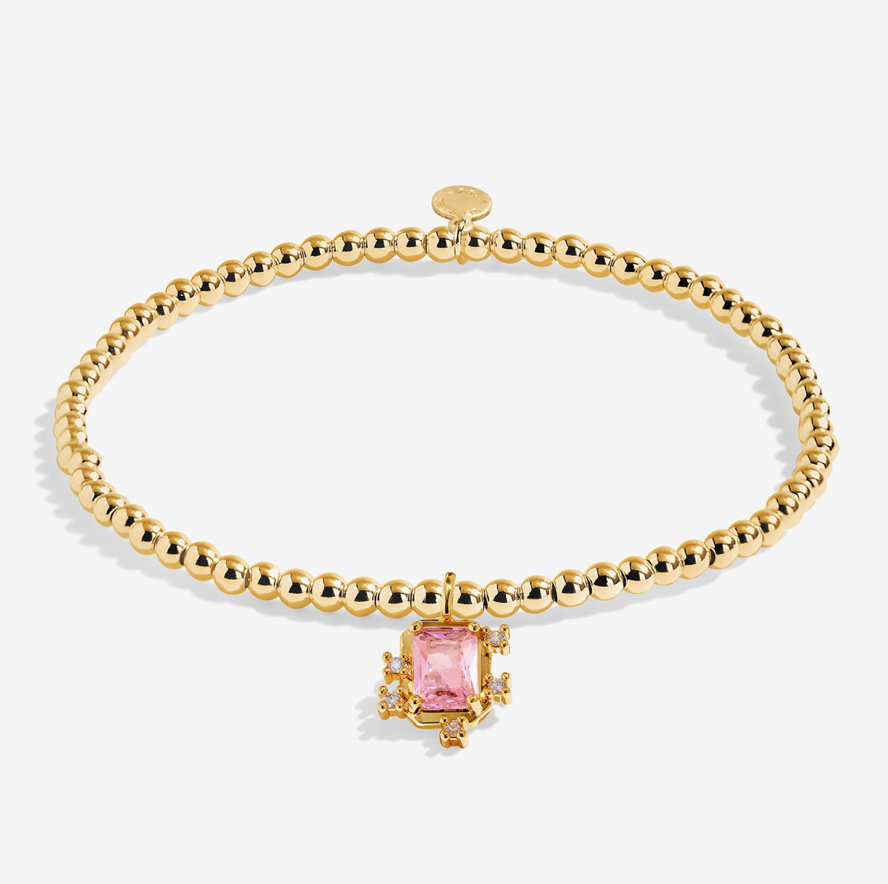 A gold beaded bracelet with a central gold-toned setting holding a rectangular pink gemstone, photographed on a clean white background. Available at Be Charmed