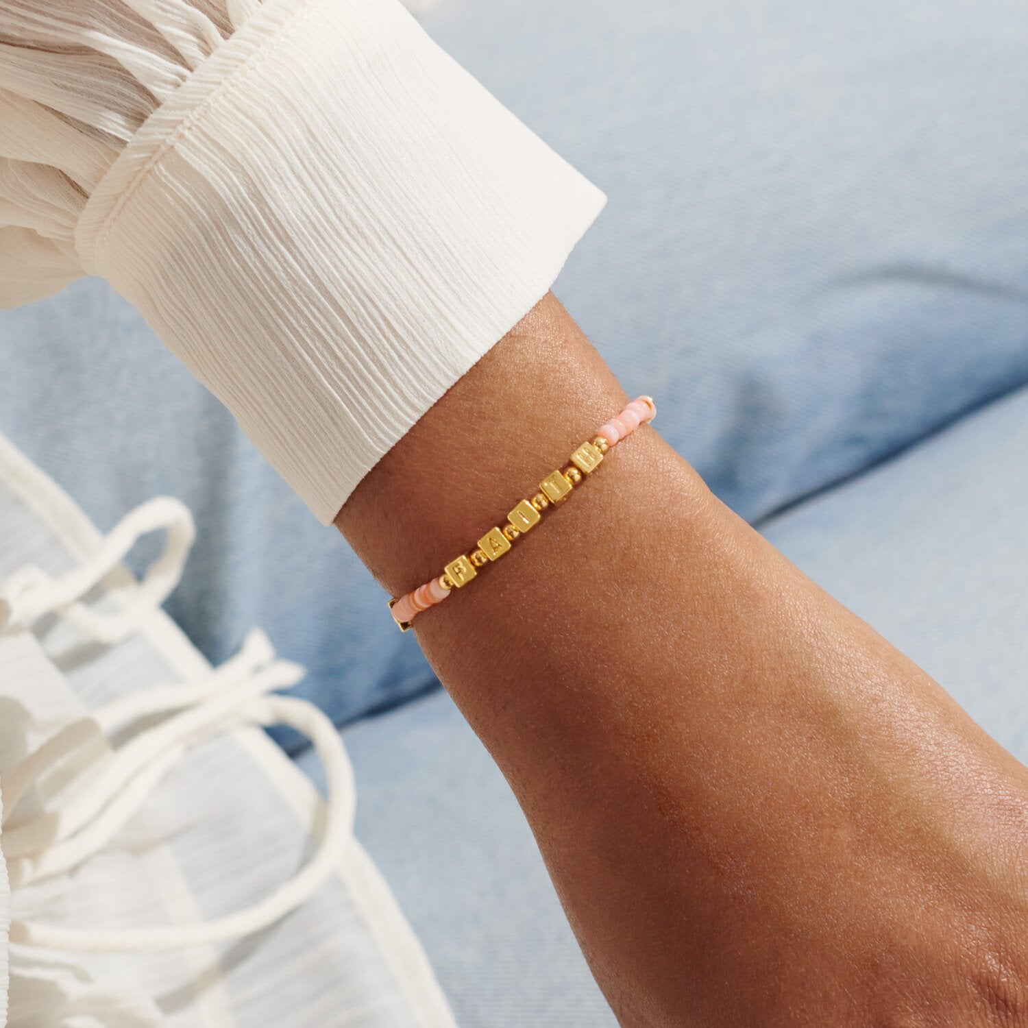 Close-up of a wrist wearing a pink beaded bracelet against a light blue background. Available at Be Charmed