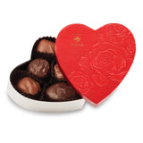 Red heart-shaped chocolate box with embossed design containing assorted chocolates on a white background. Available at Be Charmed