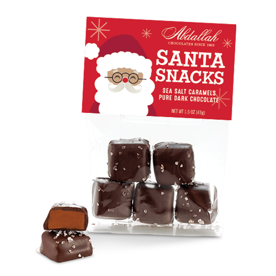 Packaging for Abdallah Santa Snacks which are sea salt caramels in dark chocolate, displayed with a Santa Claus figure in the background. Available at Be Charmed