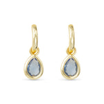 Gold earrings with teardrop-shaped blue gemstones on a white background. Avaiable at Be Charmed