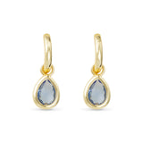 Gold earrings with teardrop-shaped blue gemstones on a white background. Avaiable at Be Charmed