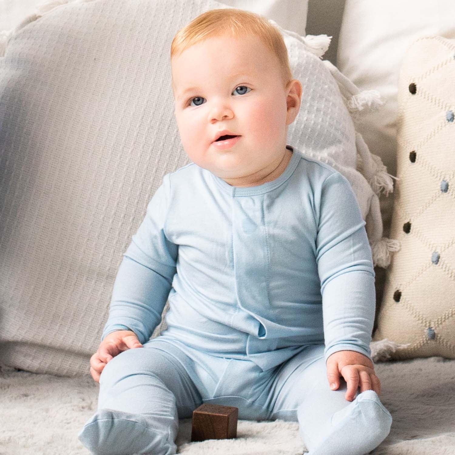 Baby wearing a Magnetic Me modal footie in Baby Blue, available at Be Charmed.
