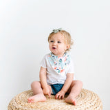 Baby wearing a Copper Pearl Leilani Bandana Bib Set bib featuring absorbent cotton front and soft fleece back, adjustable for babies 0-36 months. Available at Be Charmed.