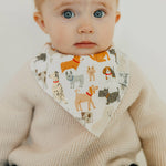 Baby wearing a Copper Pearl Rufus Bandana Bib featuring absorbent cotton front and soft fleece back, adjustable for babies 0-36 months. Available at Be Charmed.