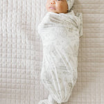 Baby wrapped with Gage print knit swaddle blanket by Copper Pearl featuring soft breathable knit fabric in neutral stripes, perfect for swaddling and tummy time—Available at Be Charmed