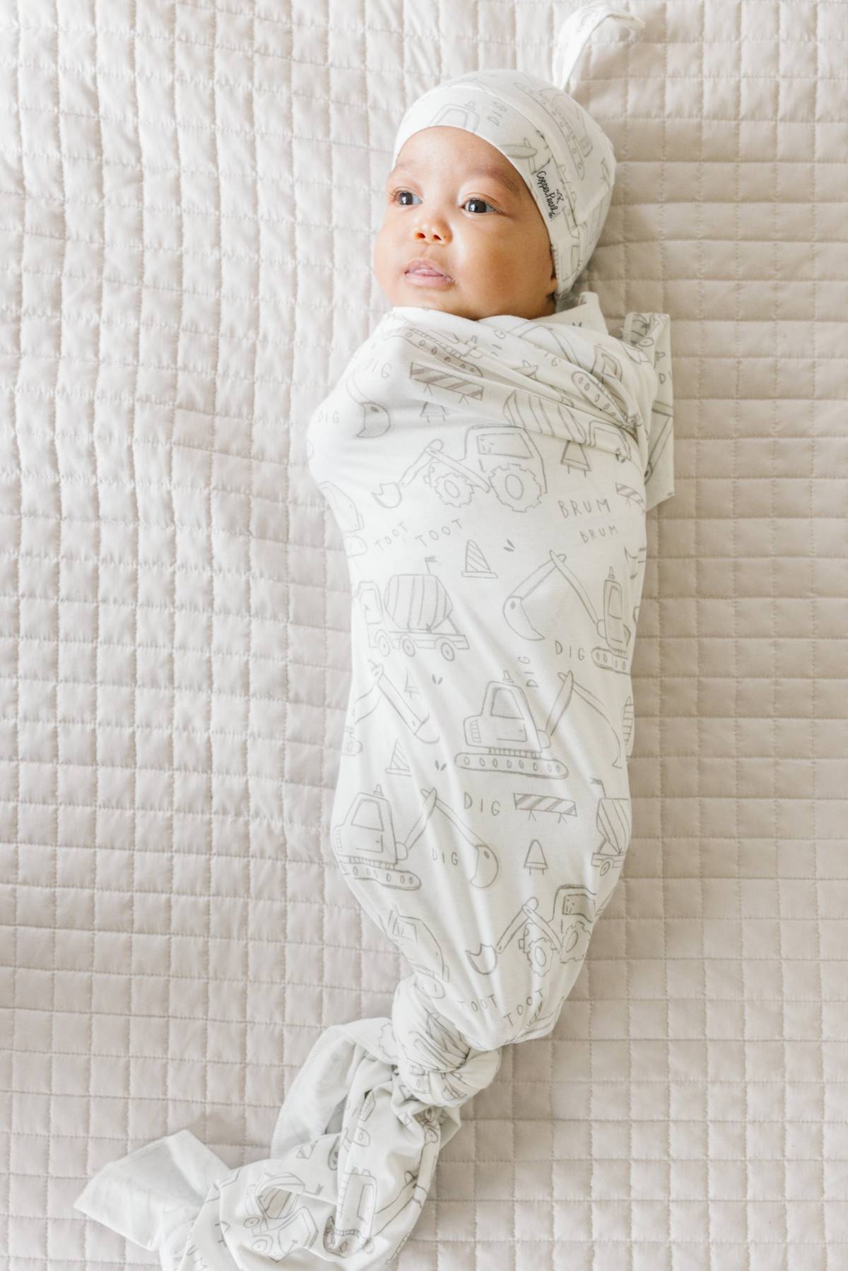 Baby wrapped with Gage print knit swaddle blanket by Copper Pearl featuring soft breathable knit fabric in neutral stripes, perfect for swaddling and tummy time—Available at Be Charmed