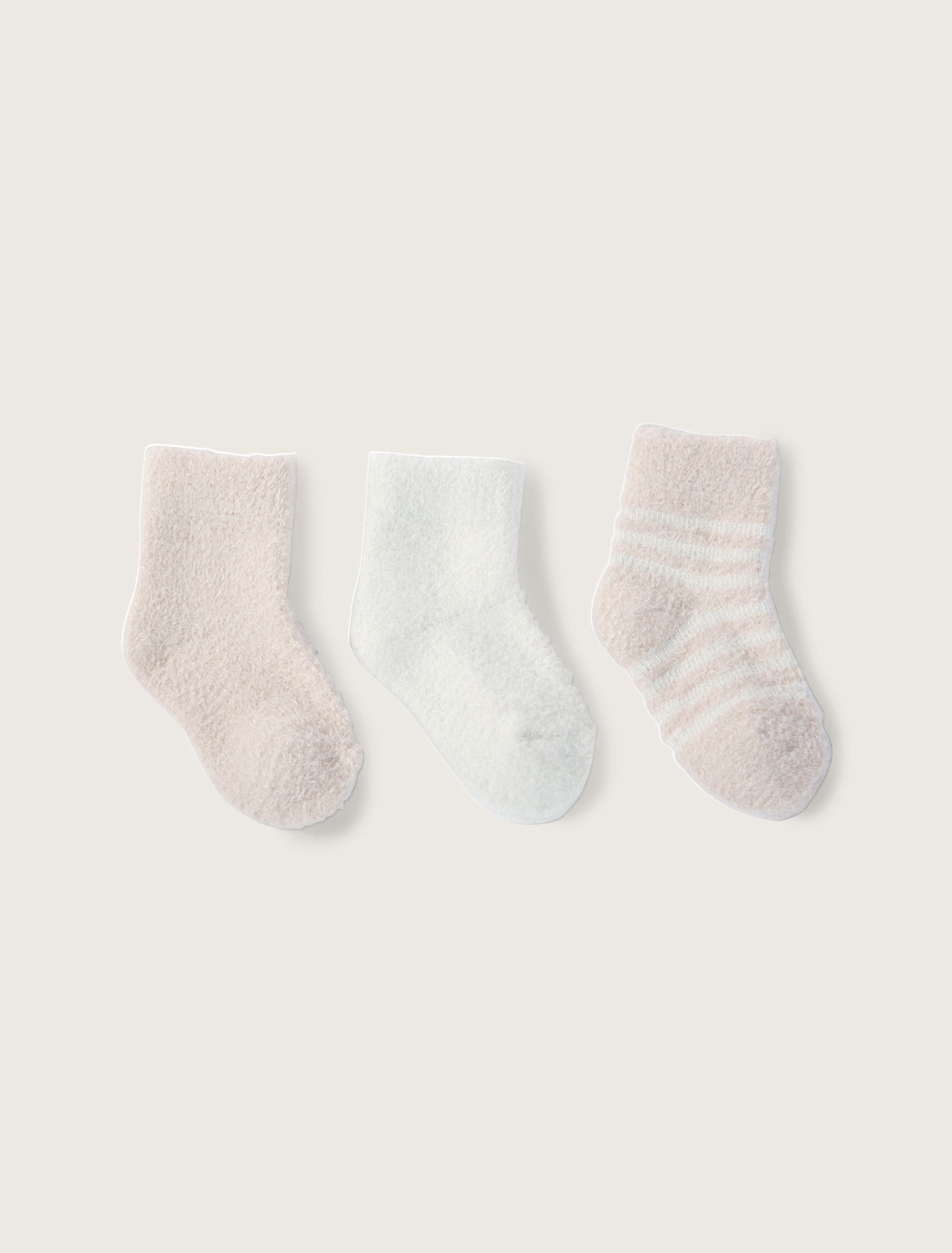 Three infant socks laid out flat, with two solid color socks in pink and pearl, and one striped sock in pink and pearl colors. Available at Be Charmed