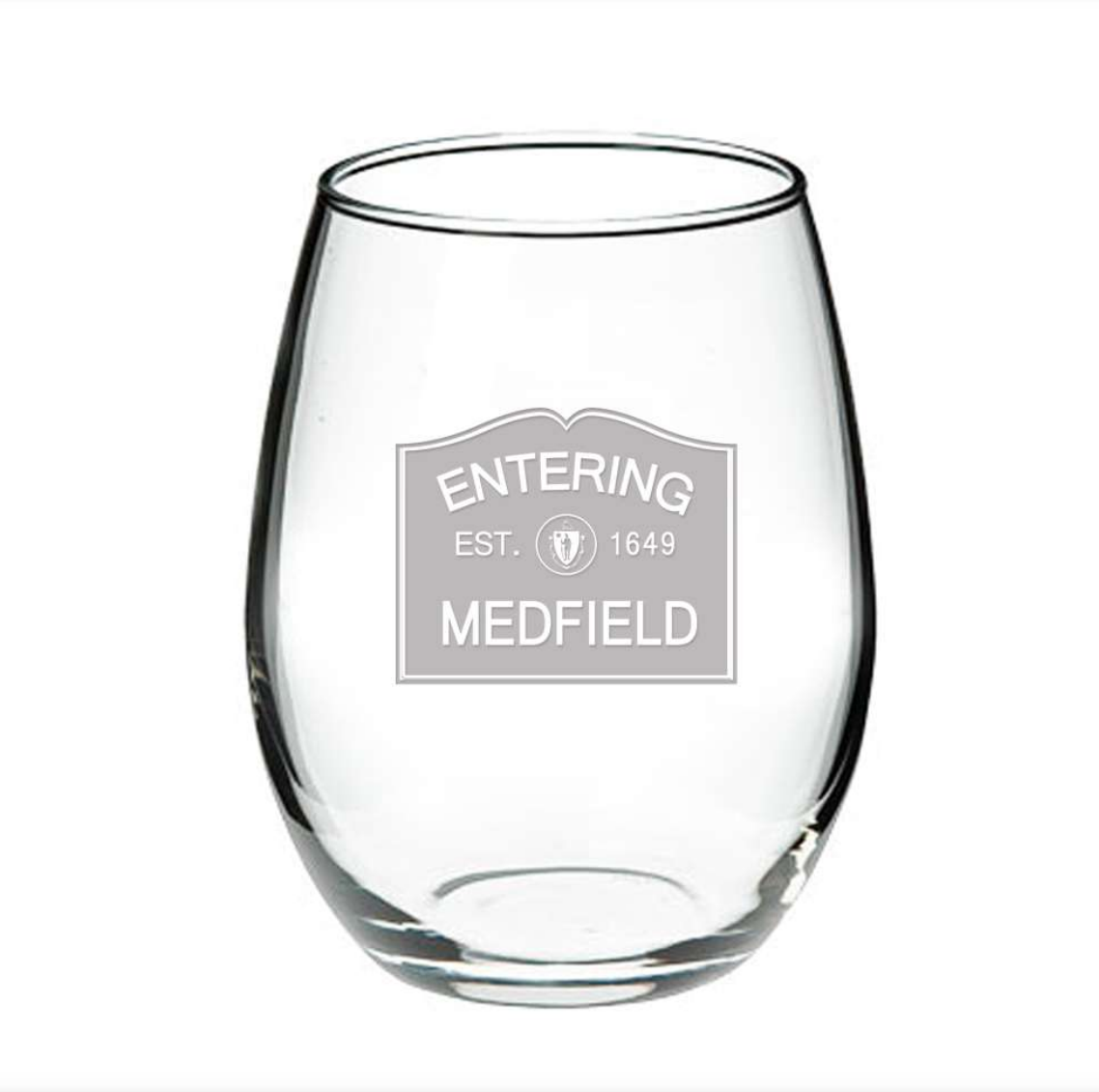 A clear glass wine glass with 'ENTERING MEDFIELD 1649' printed in black text near the base, representing the year the town was established. Available at Be Charmed