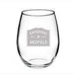 A clear glass wine glass with 'ENTERING MEDFIELD 1649' printed in black text near the base, representing the year the town was established. Available at Be Charmed