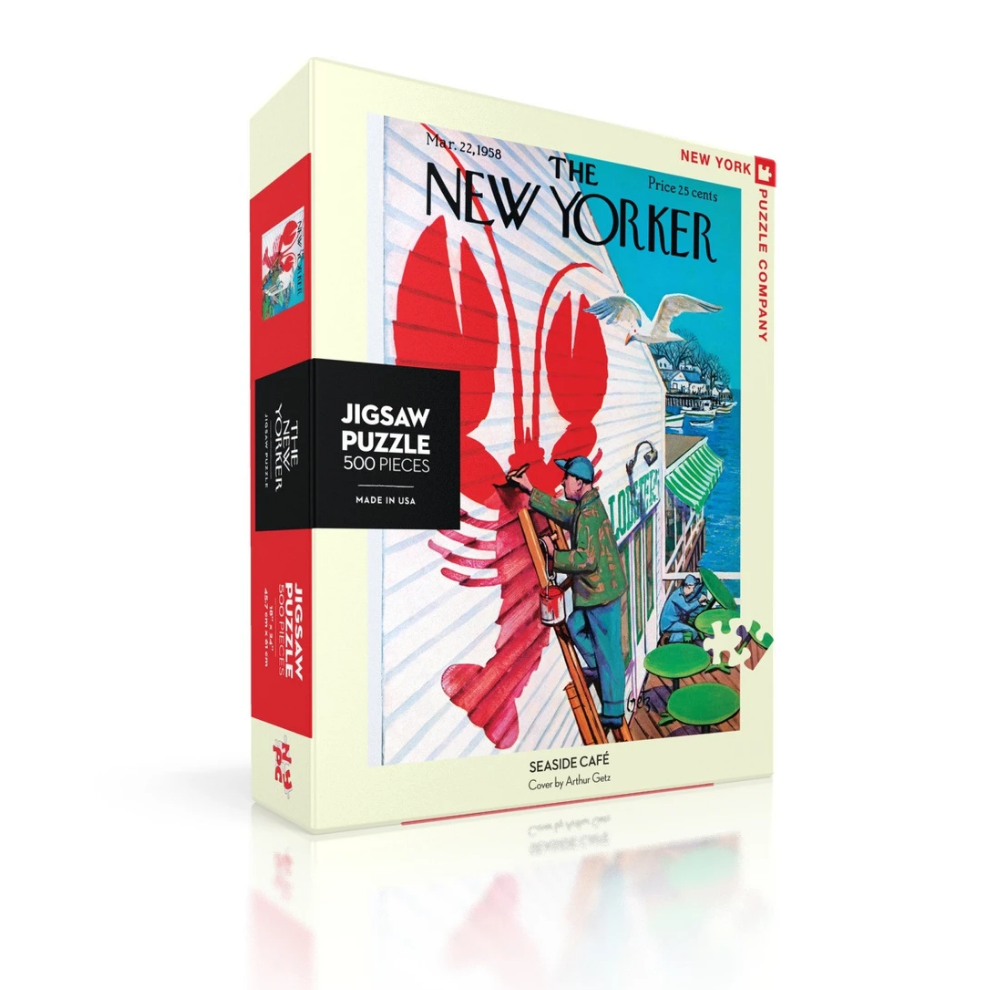 New York Puzzle Company Seaside Cafe 500 piece jigsaw puzzle featuring an illustrated harbor town cafe scene available at Be Charmed