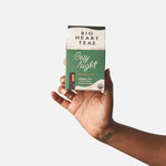 Hand holding a box of Big Heart Teas Cozy Night tea against a white background. Available at Be Charmed