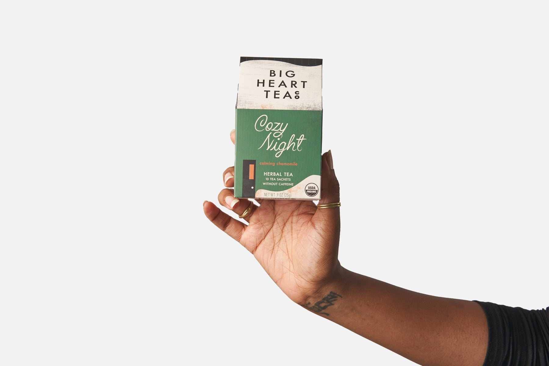 Hand holding a box of Big Heart Teas Cozy Night tea against a white background. Available at Be Charmed