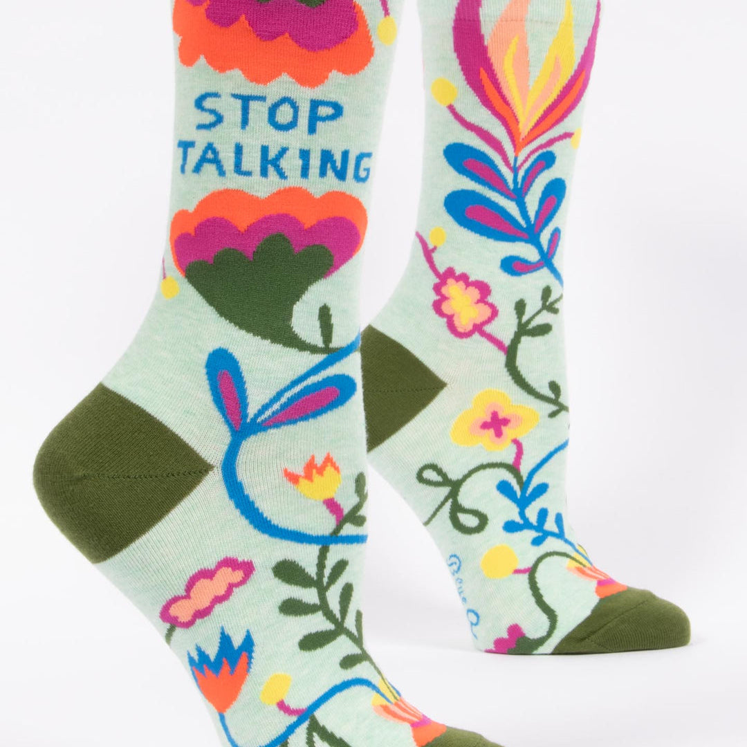 Colorful socks with floral designs and text on a light green background. Available at Be Charmed
