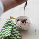 Bowl of ice cream with chocolate sauce being drizzled over it on a light surface. Available at Be Charmed