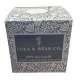 A 3-wick soy candle by Lola & Bean in a boxed container with a floral pattern. The label on the box indicates it is a 100% Soy Candle handpoured in New England. Available at Be Charmed