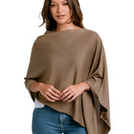 Woman wearing a brown poncho over a white shirt and blue jeans on a white background