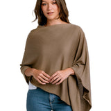 Woman wearing a brown poncho over a white shirt and blue jeans on a white background