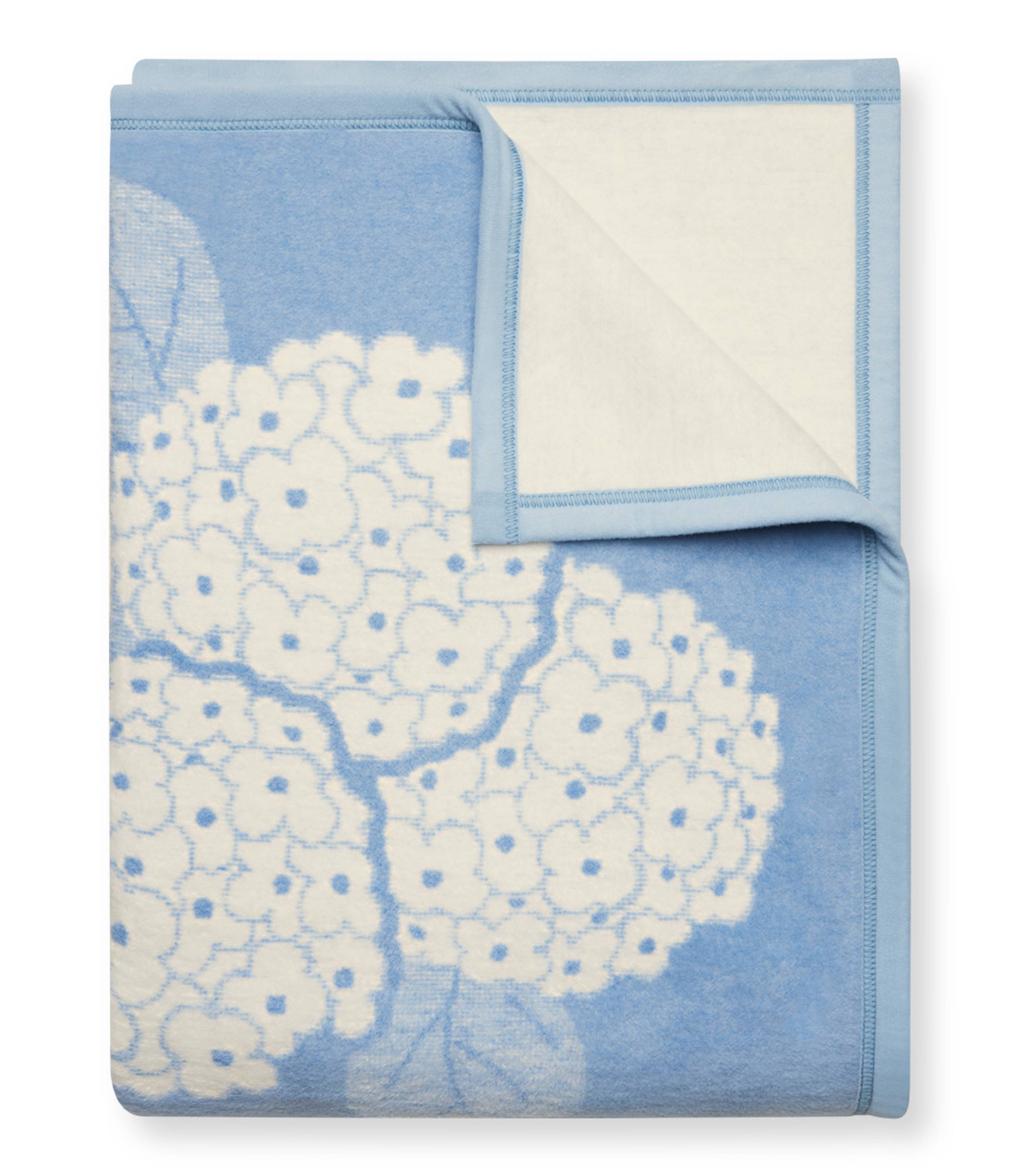 ChappyWrap Hydrangeas Bluebell Blanket featuring soft blue and lavender floral hydrangeas on a cream background. Made from a plush cotton blend for luxurious comfort and durability—ideal for garden-inspired décor or cozy lounging. Available at Be Charmed.