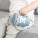 Child Holding a Bella Tunno "Juice Box Hero" Happy Sippy Cup in blue, featuring a playful design and soft, food-grade silicone, available at Be Charmed.