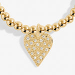 Gold necklace with a heart-shaped pendant featuring diamond-like stones on a white background. Available at Be Charmed