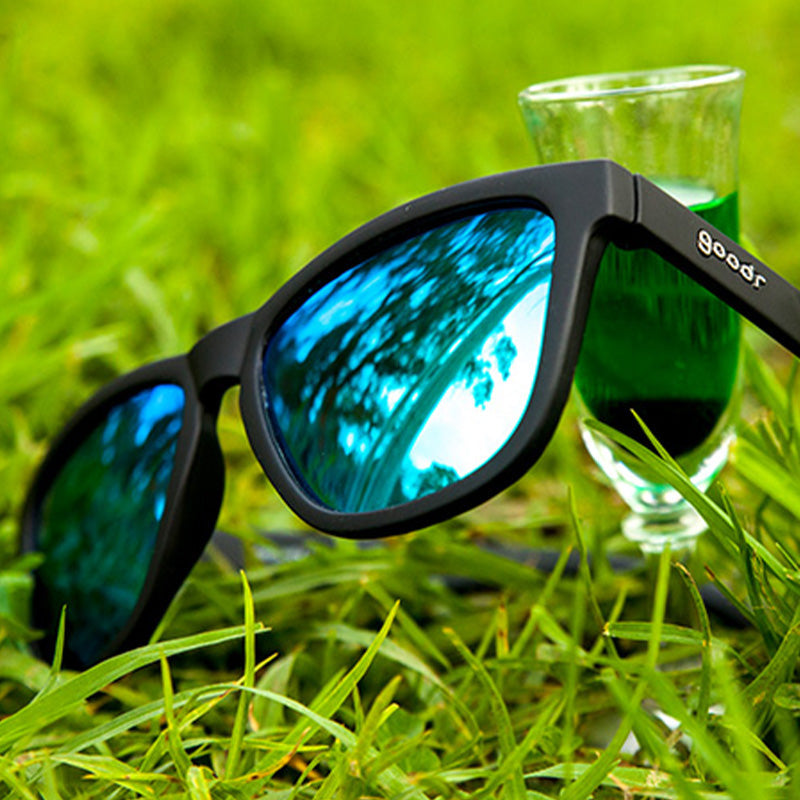 Close up on grass Vincent's Absinthe Night Terrors Goodr sunglasses with vivid green frames and polarized lenses—bold, secure, and stylish; available at Be Charmed