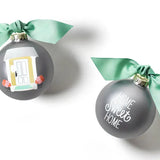 Two round glass ornaments with a hand-painted sketch of a front door on a silver background, white script, and a green accent ribbon on top. One ornament has a green bow on top. Available at Be Charmed