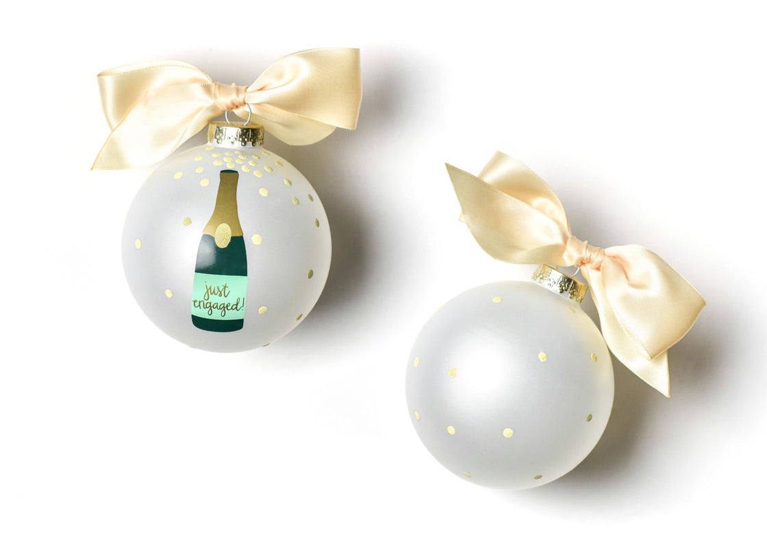 Two Christmas ornaments with champagne bottle design and gold bows on a white background. Available at Be Charmed