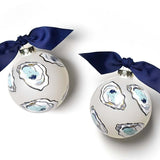 Two spherical glass ornaments with hand-drawn oysters in shades of blue and gold on a white background, adorned with navy blue bows. Available at Be Charmed
