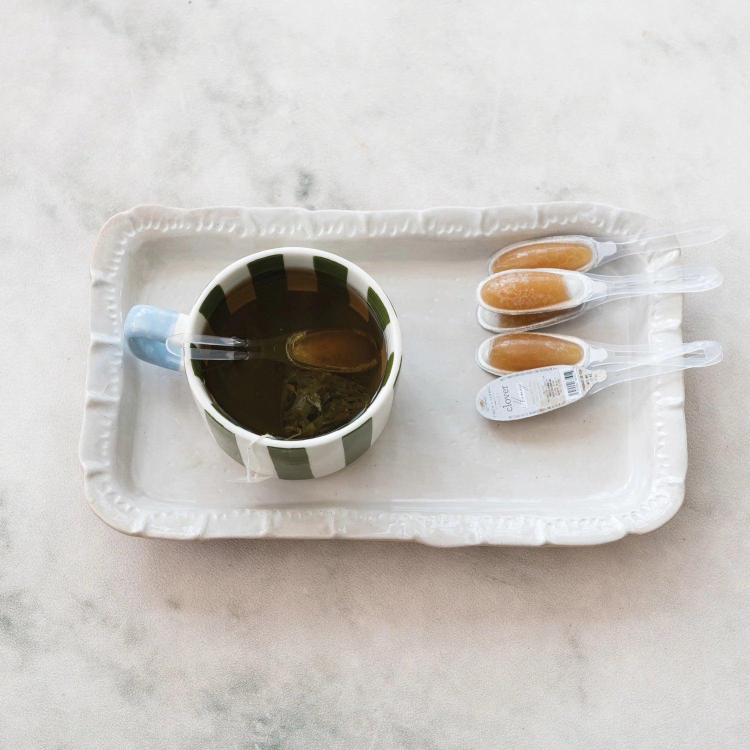 Cup of tea with honey on a white tray on a marble surface. Available at Be Charmed