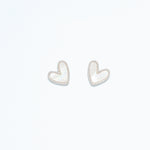 A pair of pearlized silver heart earrings on a white background. Available at Be Charmed