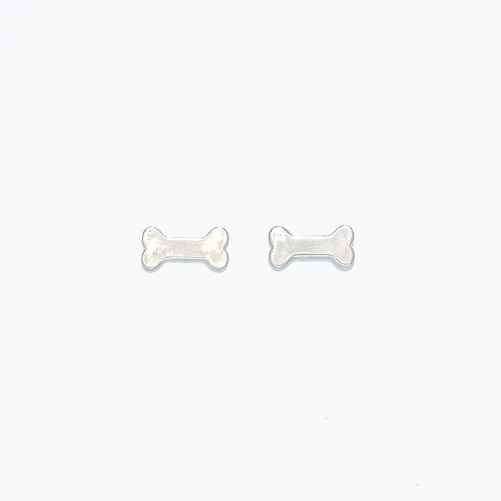 Cuties silver dog bone stud earrings featuring mini bone silhouette in polished silver-tone hypoallergenic metal with butterfly backs. Cute and lightweight accessory. Available at Be Charmed