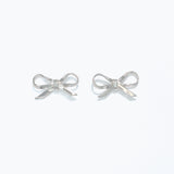 A pair of silver ribbon bow stud earrings on a white background. Available at Be Charmed