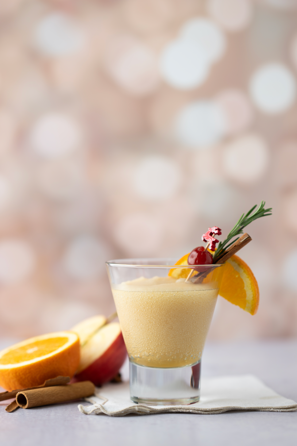 Glass of Blitzen Bourbon with garnishes on a blurred background. Available at Be Charmed.  