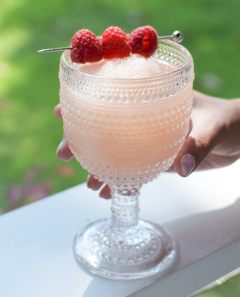 Glass full of D'Marie Frosé Slush Mix pouch featuring fruity pink design—craft cocktail mix to combine with rosé wine and freeze. Light, refreshing, and easy. Available at Be Charmed