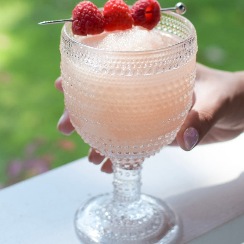 Glass full of D'Marie Frosé Slush Mix pouch featuring fruity pink design—craft cocktail mix to combine with rosé wine and freeze. Light, refreshing, and easy. Available at Be Charmed