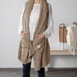 Demdaco Giving Shawl in camel (27″×70″), buttery‑soft fabric with two pockets—giftable hug, available at Be Charmed.